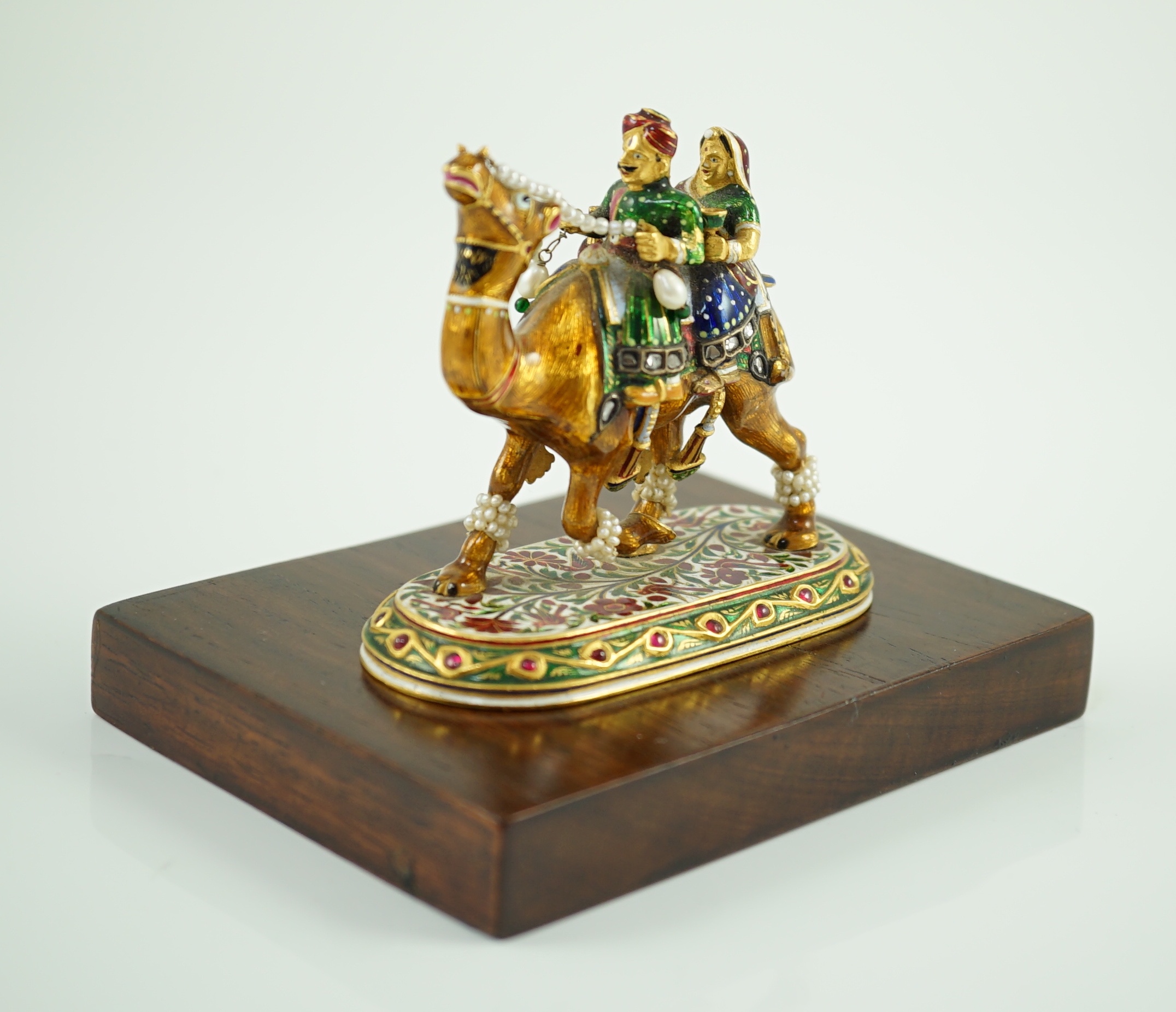 A 20th century Indian Mughal style gold, polychrome enamel, diamond, seed pearl and cabochon ruby set miniature model of a camel with two riders, on oval base